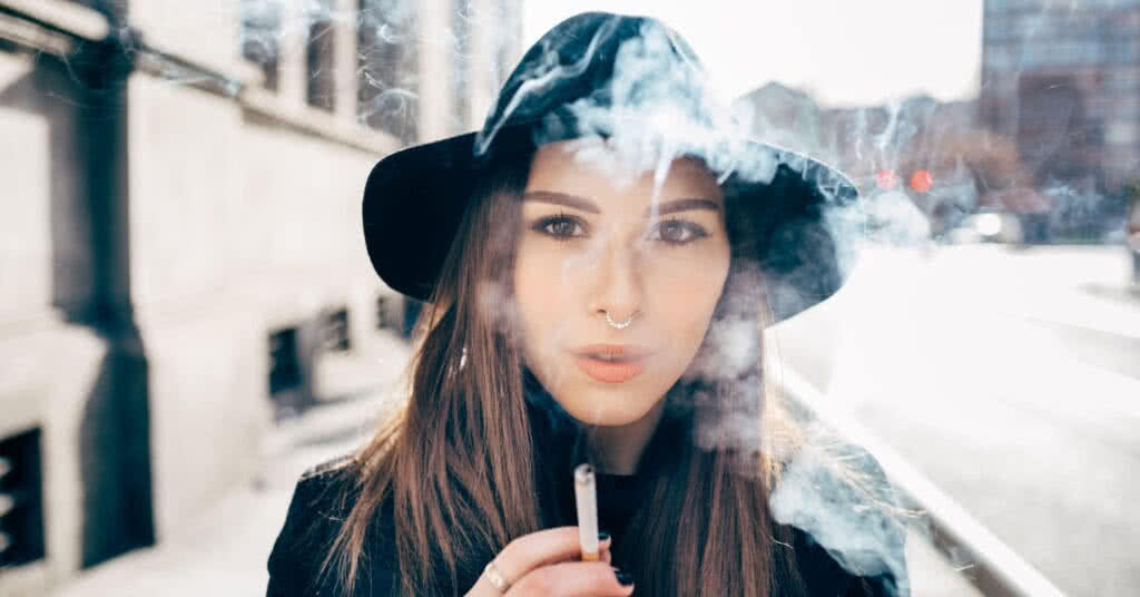 Jovem mulher caucasiana ao ar livre, sorrindo e feliz. Imagem ilustrativa para o artigo "Fumar causa varizes?" no site Vascular.pro.