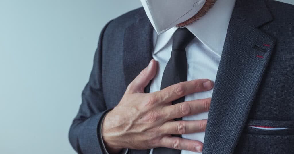 Homem elegante de negócios com máscara respiratória KN95 protetora e sintomas de dor aguda no peito, possivelmente relacionados ao aneurisma da aorta.