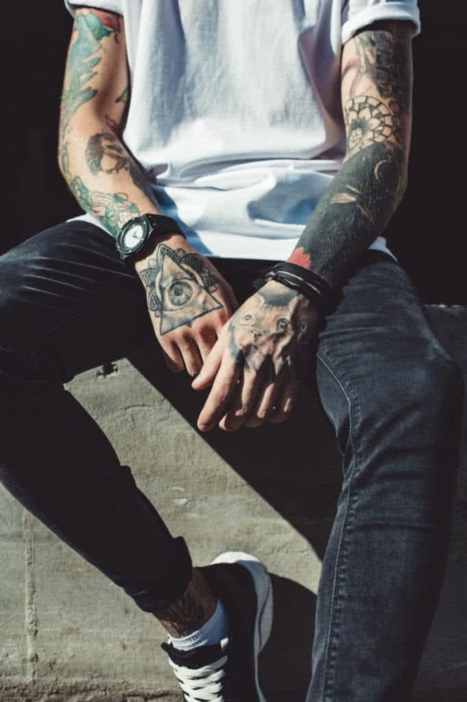 Imagem de um homem tatuado do lado de fora, ilustrando a relação entre tatuagem masculina e saúde. A tatuagem é uma forma de expressão artística, mas é importante lembrar que ela também pode afetar a saúde da pele. É fundamental escolher um tatuador profissional e seguir as orientações de cuidados pós-tatuagem para evitar complicações.