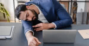 Imagem de um empresário exausto dormindo no local de trabalho. Descubra as principais causas e tratamentos eficazes para a fadiga crônica e aprenda a vencê-la.